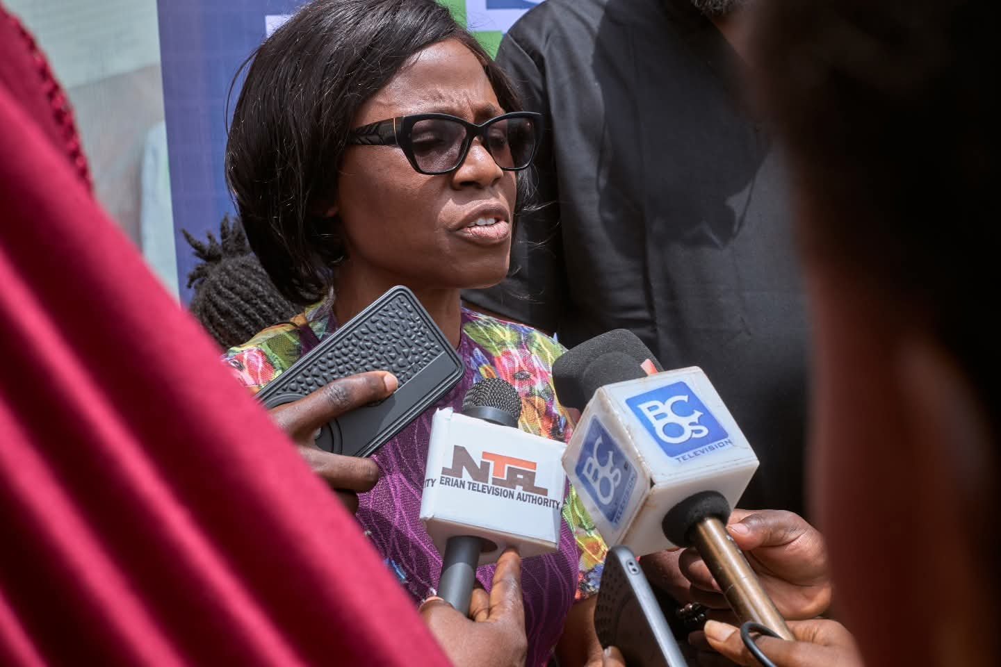A woman speaks to reporters holding television microphones.