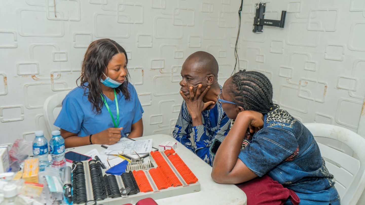 An eye care clinician consults with a man at a table of eye-testing lenses.