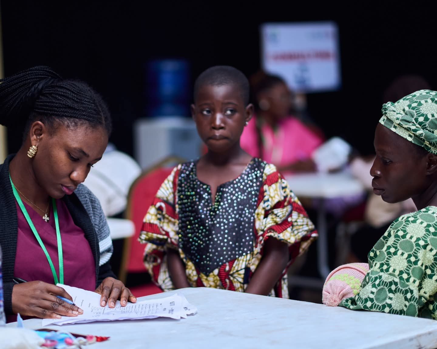 A volunteer writes on a form as a woman and child wait at a table.