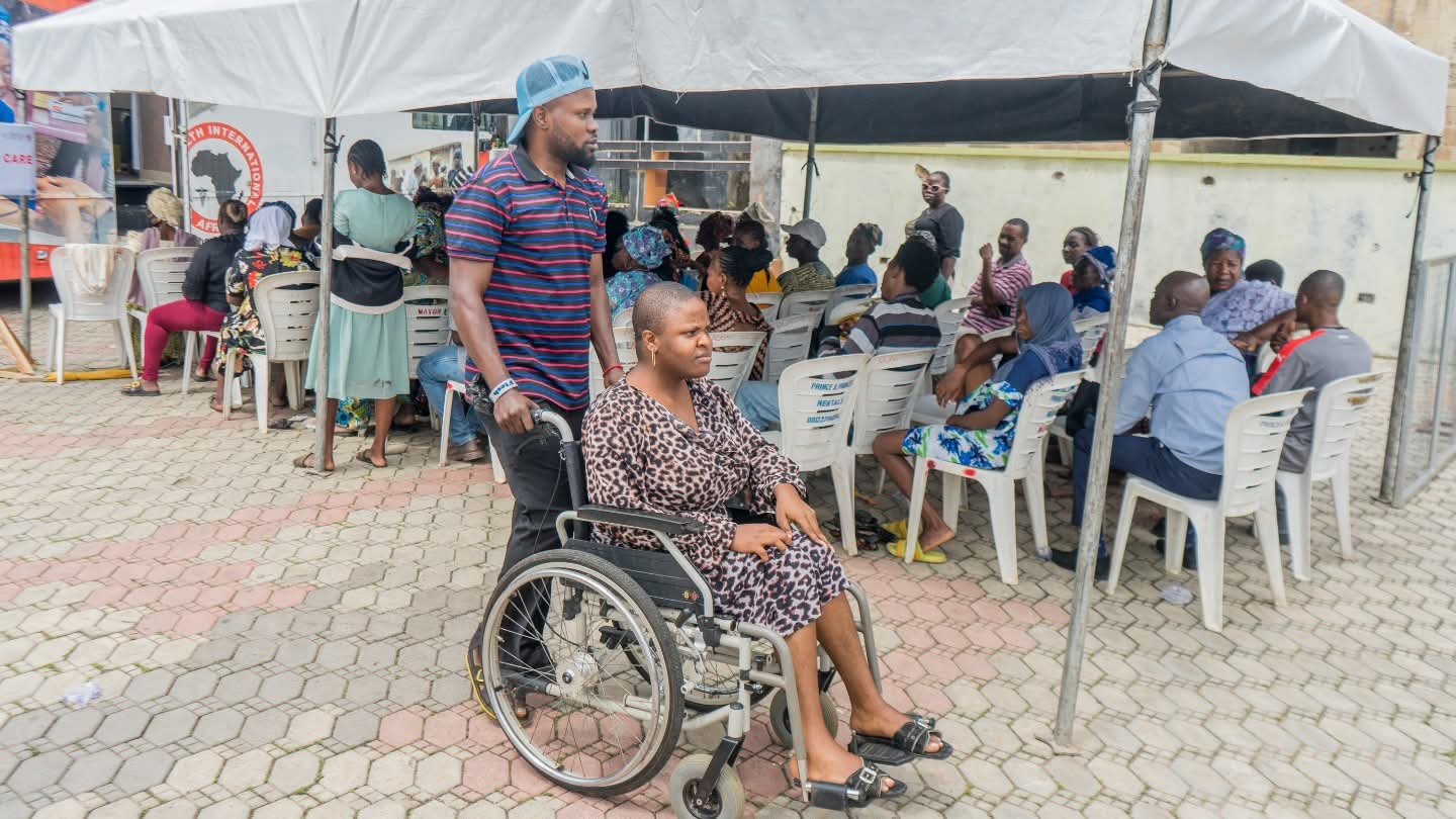 A volunteer pushes a wheelchair participant under an outreach tent.